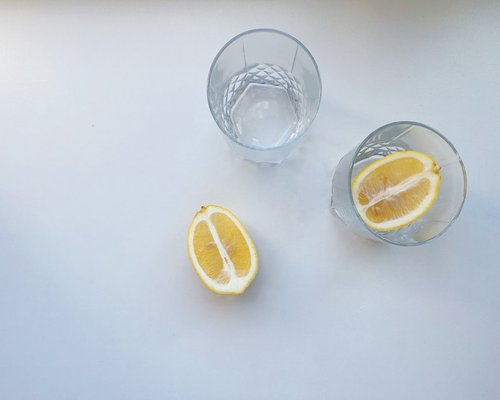 A glass of fresh water with lemon slices on a bright desk